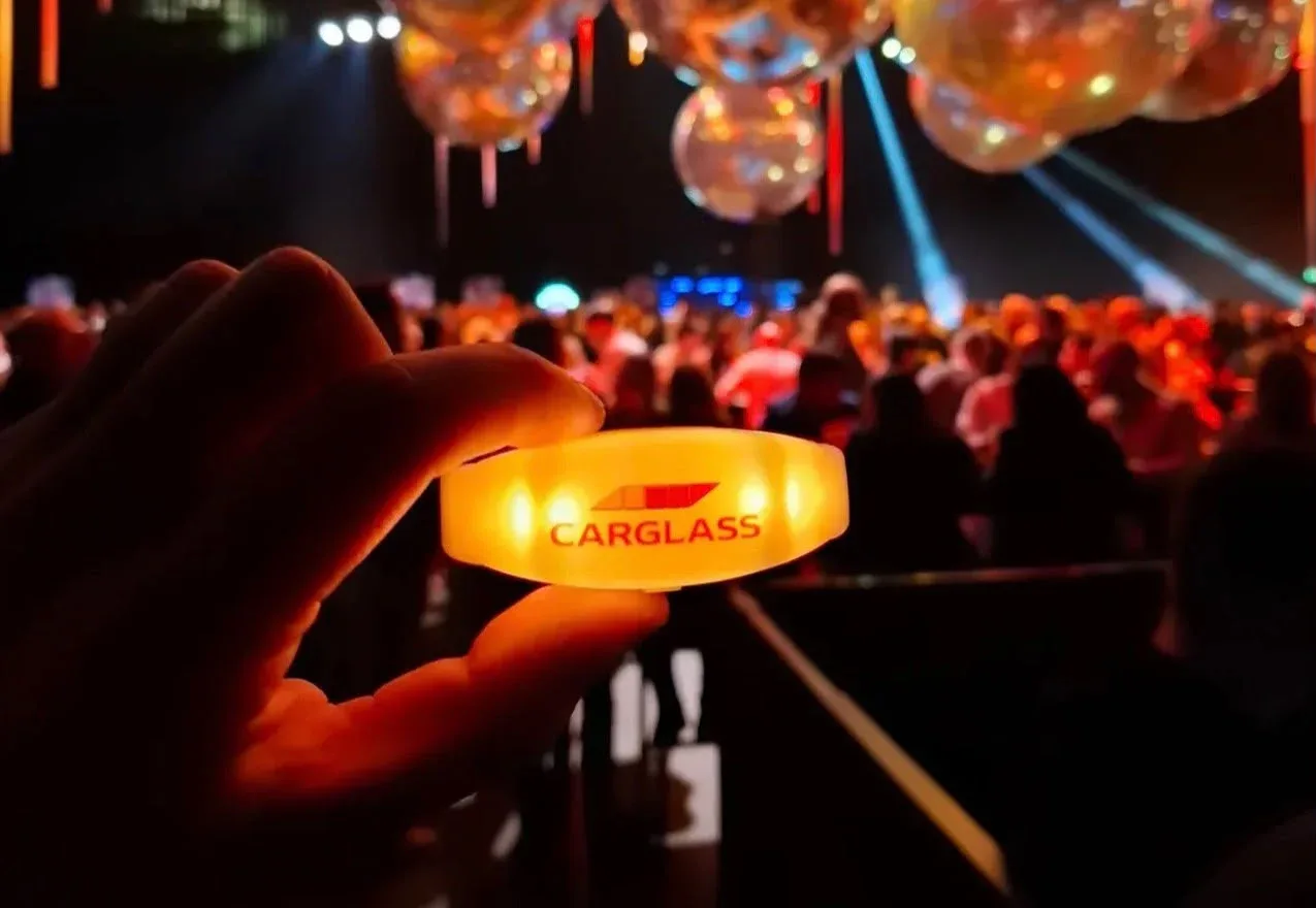 A guest holds up a glowing amber wristband printed with the Carglass logo at the company party