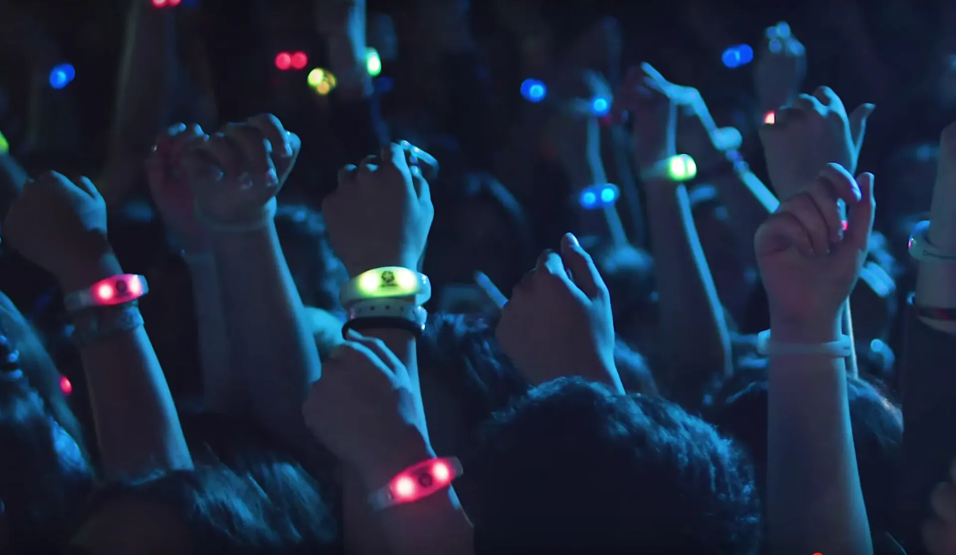 Raised fists in a concert crowd, LED wristbands glowing on every wrist