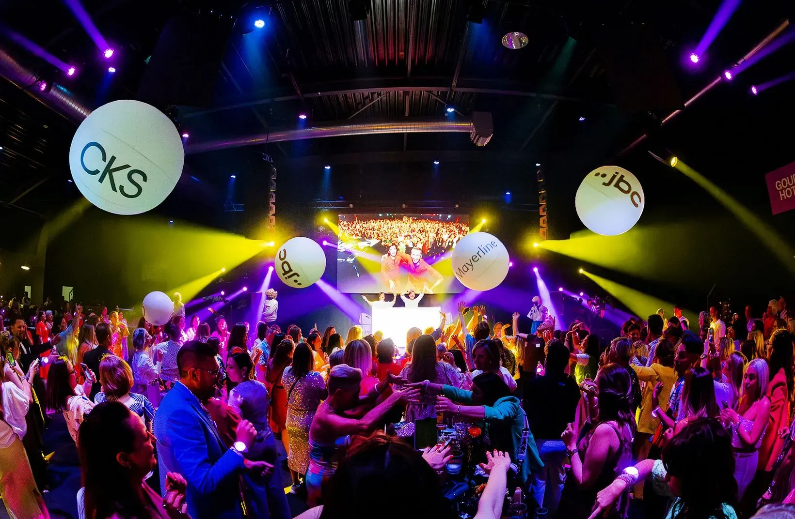 CKS and JBC Mayerline staff dance under giant LED balls, wristbands on their wrists