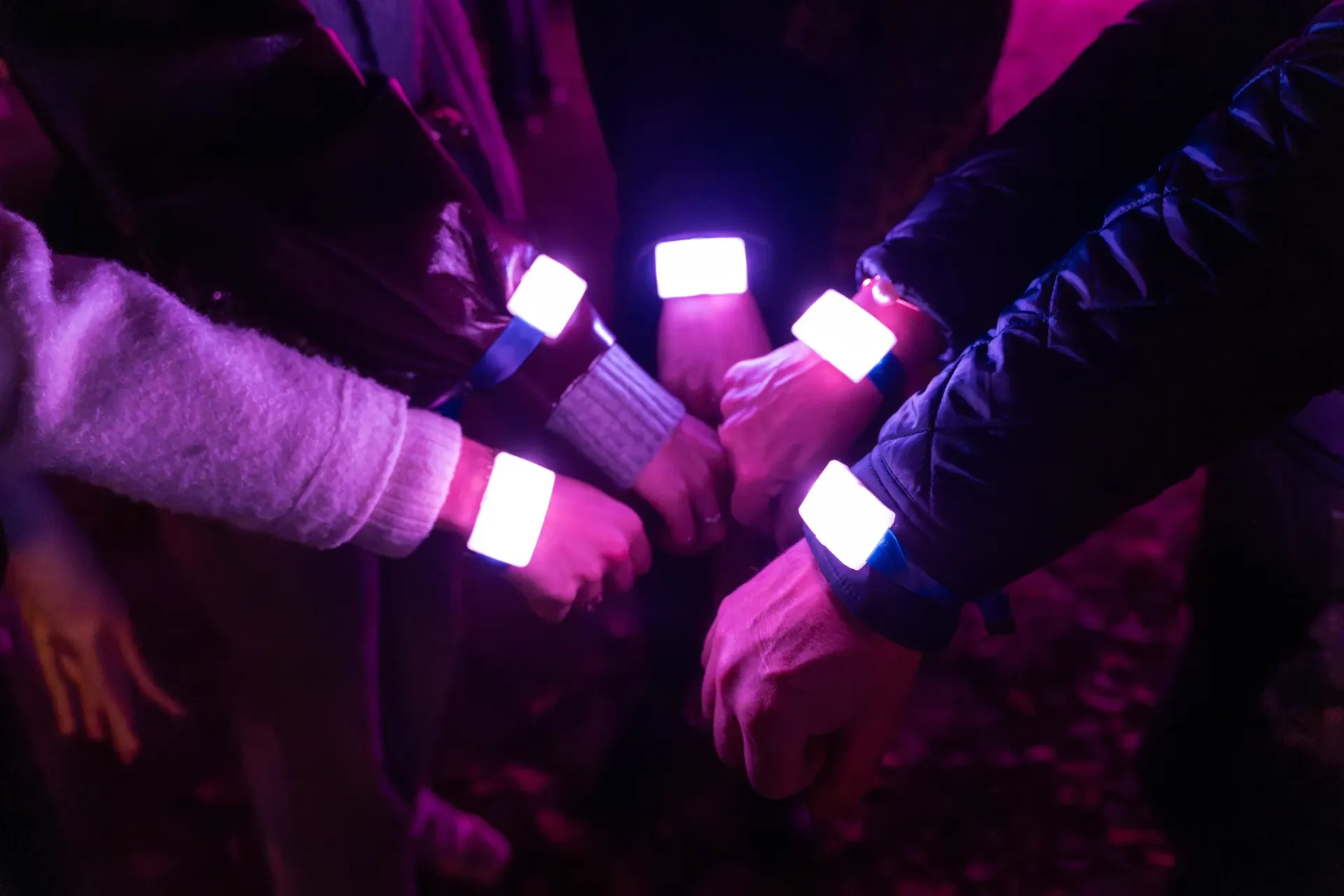 Visitors at a light festival join hands, their wristbands lit magenta