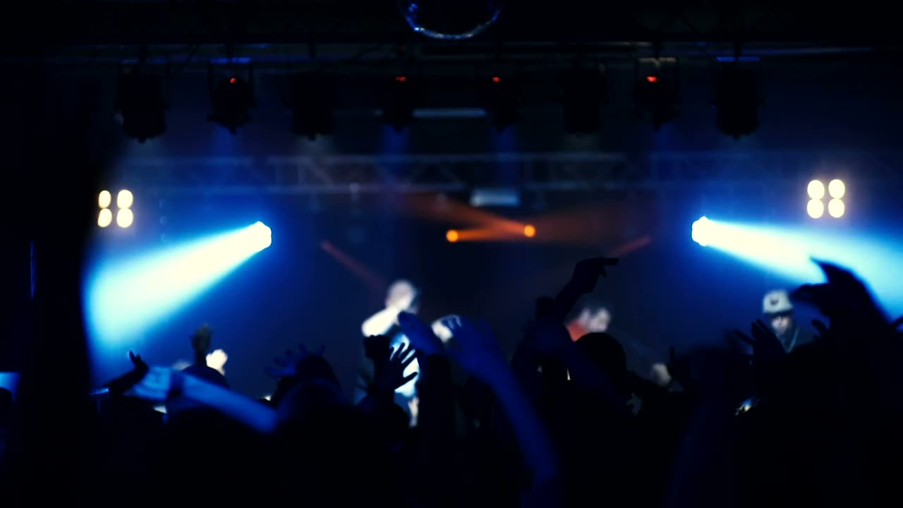 A concert crowd with hands raised under blue and red stage light